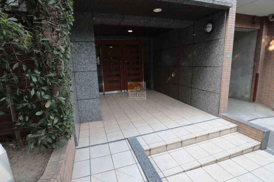 セザール第３鷺ノ宮エントランス2｜重厚な石張りの壁面に囲まれたエントランスは、控えめながら品格を感じさせます。両開きの木目調扉は、防犯性とデザイン性を両立しています。帰宅のたびに、安心感と静けさに包まれる感覚があります。