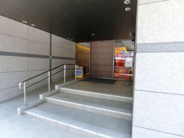 後楽園ビューハイツ外観共用部1｜エントランスです。スロープが設置されています。耐震適合を示す青いシールがあります。エントランスは自動ドアになっています。