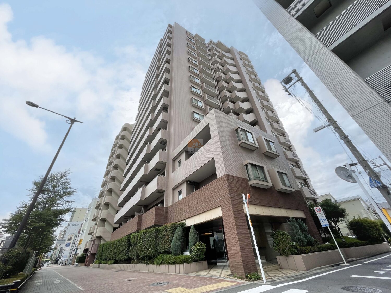 クリオ要町壱番館の角地側外観。低層部にはブラウンのタイルと豊かな植栽があしらわれ、重厚感と落ち着きのある佇まい。駅近ながら、プライバシー性を感じられる立地です。クリオ要町壱番館は、平成16年築、15階建てのマンションです。
