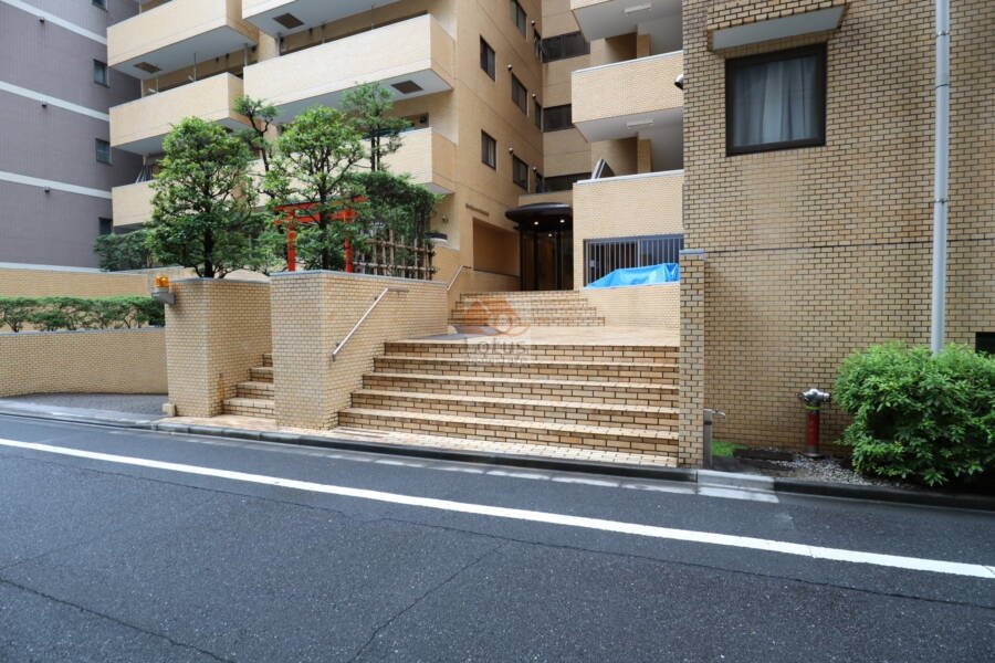 ライオンズマンション箱崎町エントランス1｜階段を上がるとエントランスがあり、その周囲には緑が植えられています。マンションの前には、小さな鳥居が立っており、落ち着いた街並みに溶け込んでいます。