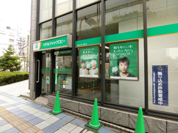 コスモ金町壱番館アプローチ6｜通りを渡るとりそな銀行が見えます。これを南西（都心方面）に向かいます。ムロツヨシさんのポスターがたくさんお出迎え。