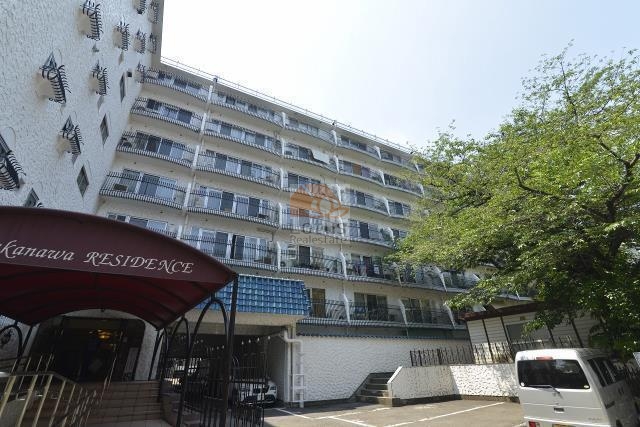 白い外壁と黒のバルコニー手すりが整然と並ぶ外観で、青い屋根がアクセントとなっています。前面にはエントランスに向かう車寄せスペースと樹木が見られます。秀和高輪レジデンスは、昭和45年築、7階建てのマンションです。