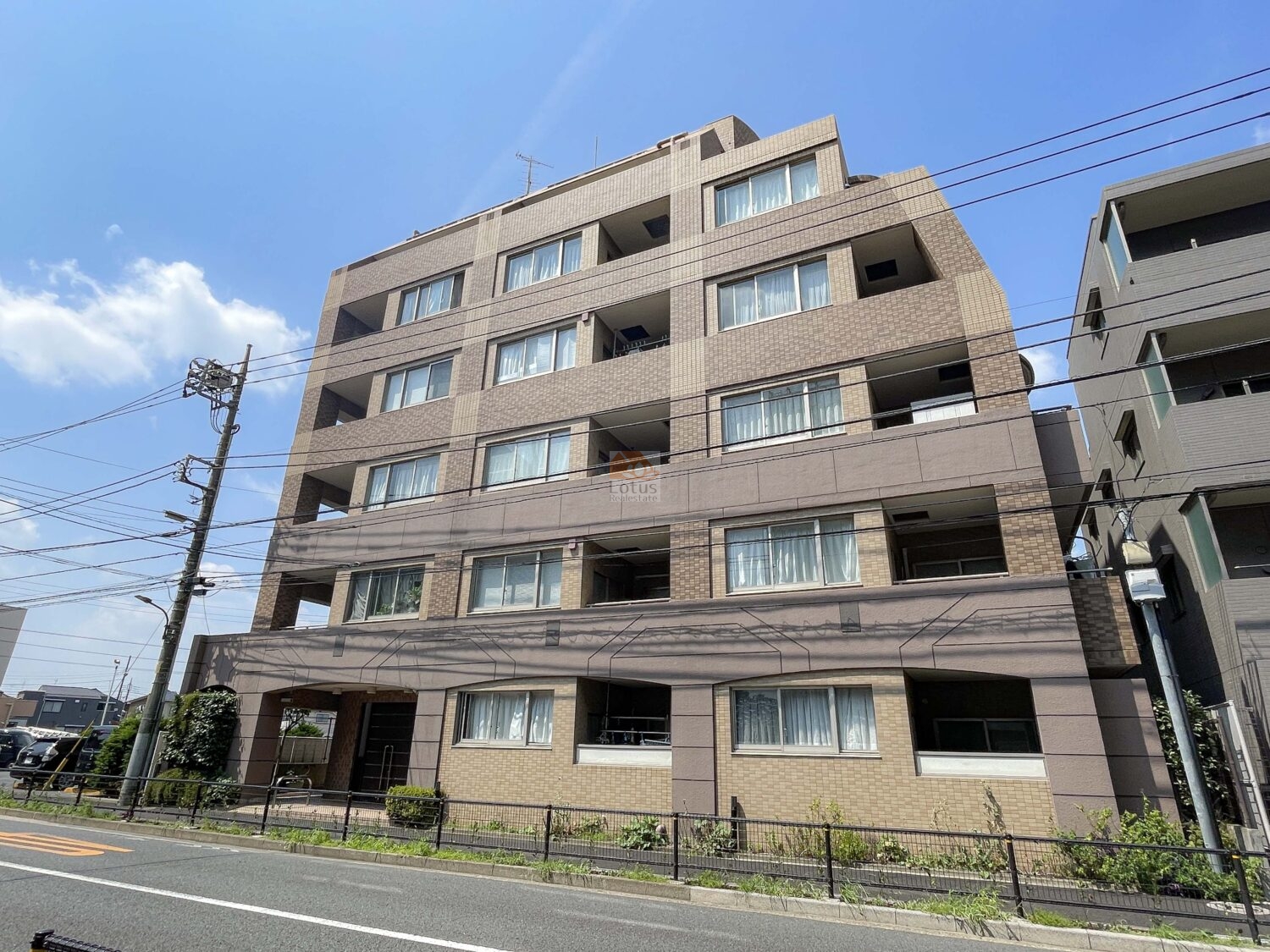 落ち着いたブラウンタイルの外観が印象的な建物です。富士街道に面し、直線的なラインが整ったファサードが都市的な印象を与えます。手前の植栽やフェンスが整備され、道路との境界がすっきりと保たれています。グランシティ武蔵関は、平成11年築、7階建てのマンションです。