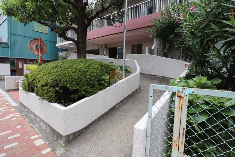 東陽町スカイハイツエントランス2｜エントランスへ続く白いスロープは曲線状に配置され、周囲には植栽が多く整えられています。