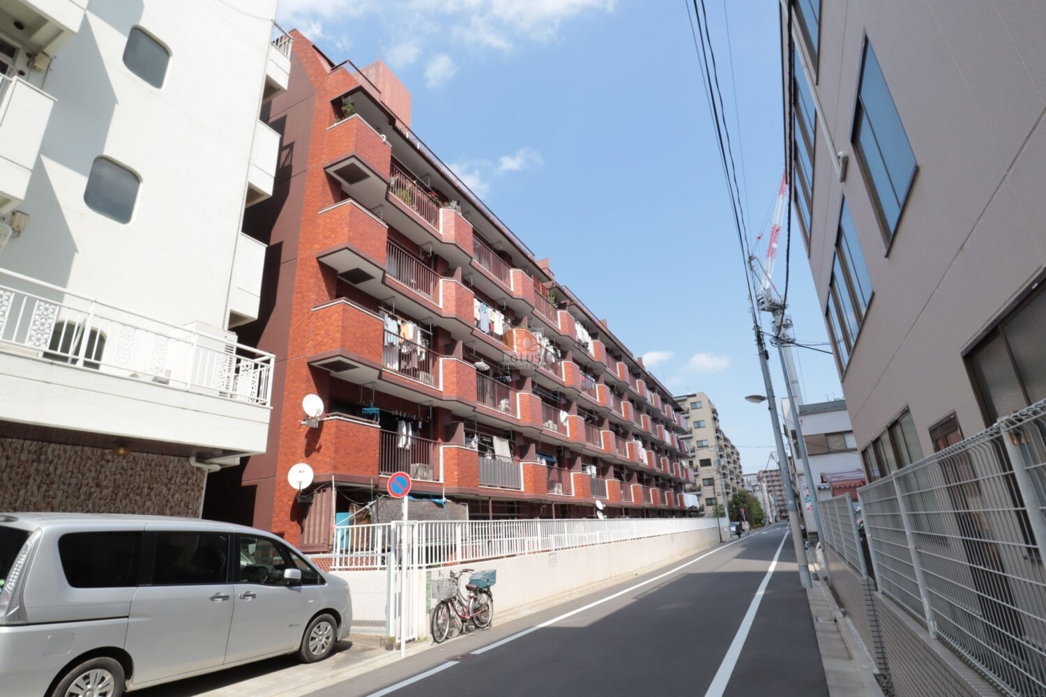 シャンボール尾久の外観です。赤茶のタイル貼りが印象的で、どこか懐かしい温かみを感じるデザインです。通りに面してバルコニーが並び、生活の息づかいが街に溶け込んでいます。青空に映える姿は、年月を重ねた風格を感じます。