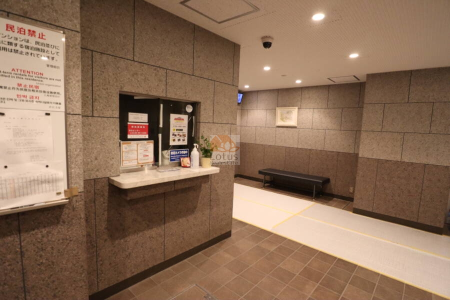 日本橋箱崎ハイツ共用部1｜管理人室の窓口が設けられ、各種掲示物とともに住まいの管理が感じられる空間です。照明が明るく、防犯カメラも見受けられます。