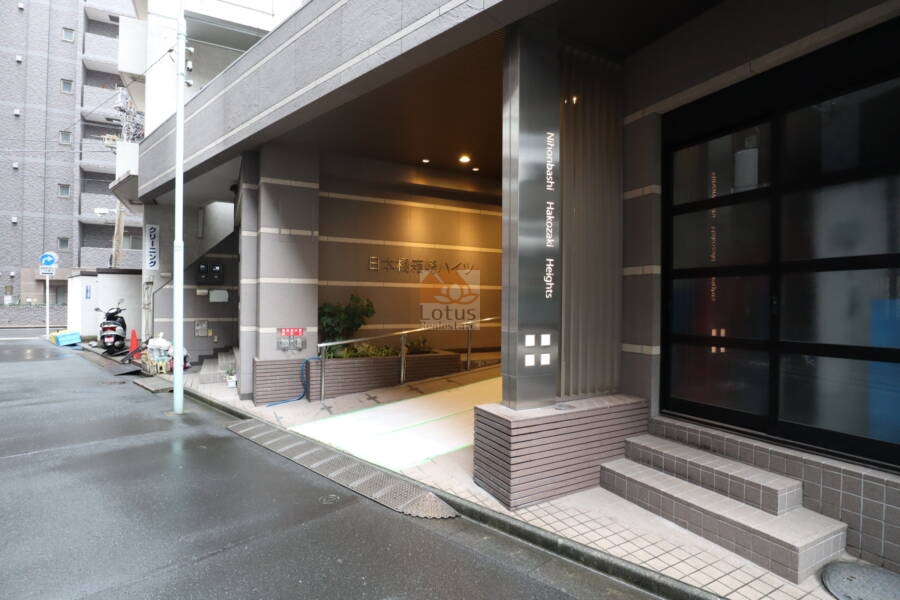 日本橋箱崎ハイツエントランス1｜エントランス前です。植栽を配したスロープ付きのアプローチがあり、歩行補助にも対応しています。正面には物件名のサインがあり、外観の印象を引き締めています。