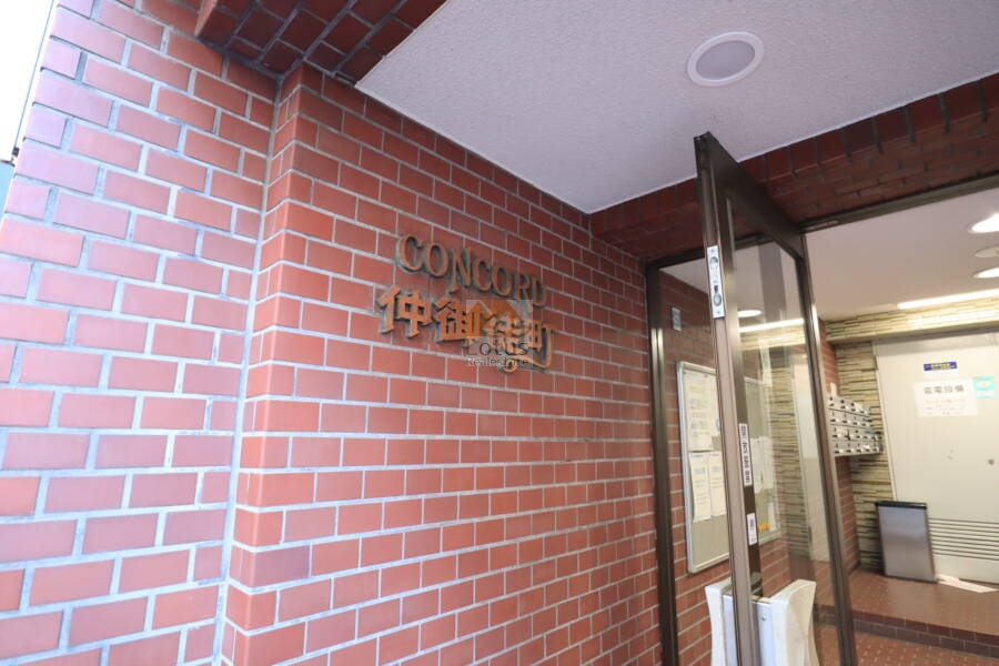 コンコード仲御徒町エントランス1｜「CONCORD 仲御徒町」のサインプレートが赤煉瓦の壁に浮かび上がる正面玄関まわり。控えめながら、確かな存在感を感じさせるエントランスです。