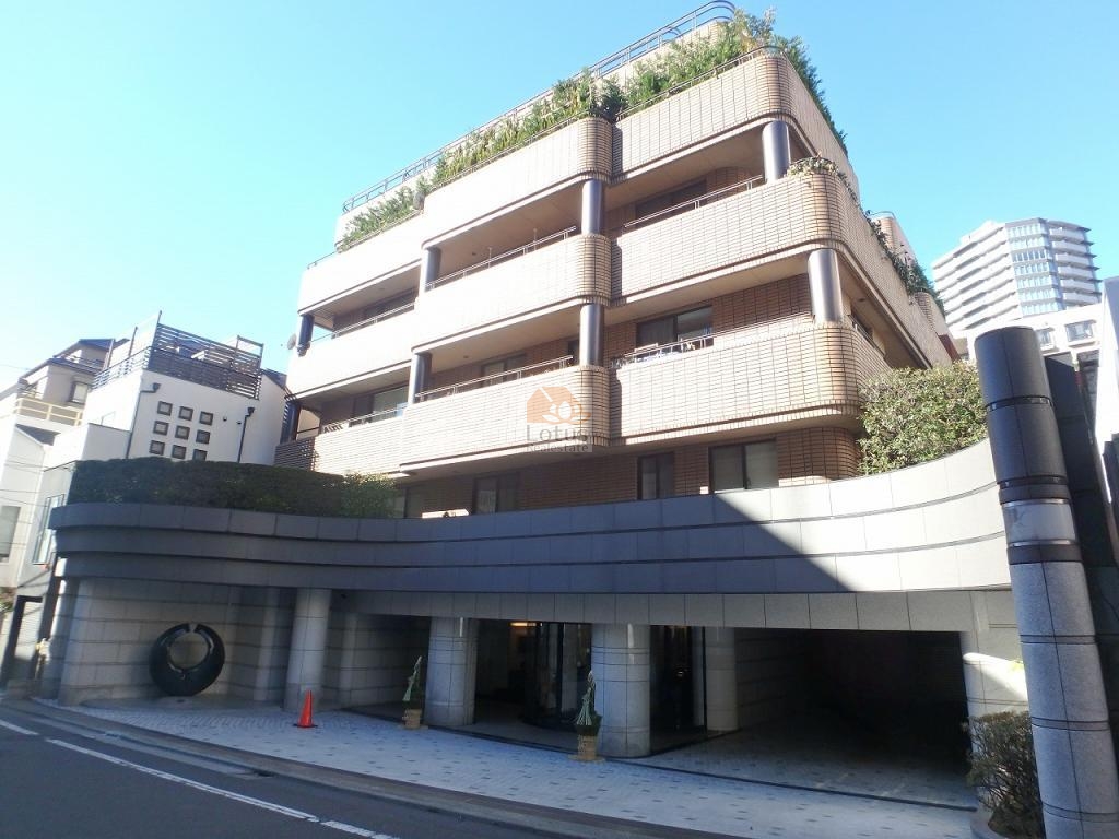 ベルテ西参道の外観。ベージュ系のタイル外壁に、丸柱と曲線的なバルコニーが層を成して連なっています。前面には曲面の石張り壁が伸び、その下に車寄せ状のピロティが設けられています。屋上部と各バルコニーの縁に植栽が見え、通りからエントランスまでの動線が陰影のある庇で区切られています。ベルテ西参道は、平成１年築、７階建てのマンションです。