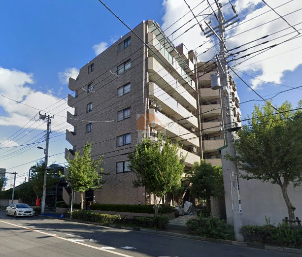 レクセルマンション竹ノ塚の外観。落ち着いたタイル張りの外壁と、角に広がる植栽が街並みにやさしく溶け込んでいる。駅から少し離れた静かなロケーションで、落ち着いた暮らしをイメージさせる建物構成。レクセルマンション竹ノ塚は、平成8年築、9階建てのマンションです。
