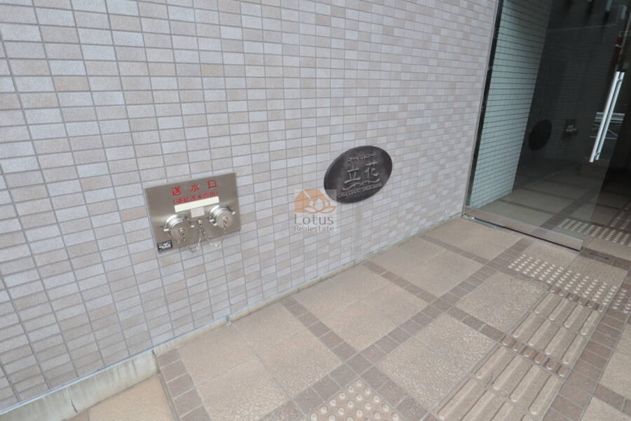 オーバルコート立花エントランス2｜館銘板が設置され、建物名がはっきりと確認できます。植栽と外壁の素材が、落ち着いた印象を与えます。