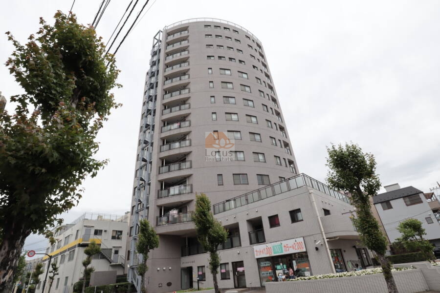 オーバルコート立花外観2｜外観はガラス面が目を引くバルコニー構造が特徴です。植栽スペースと歩道も整えられています。