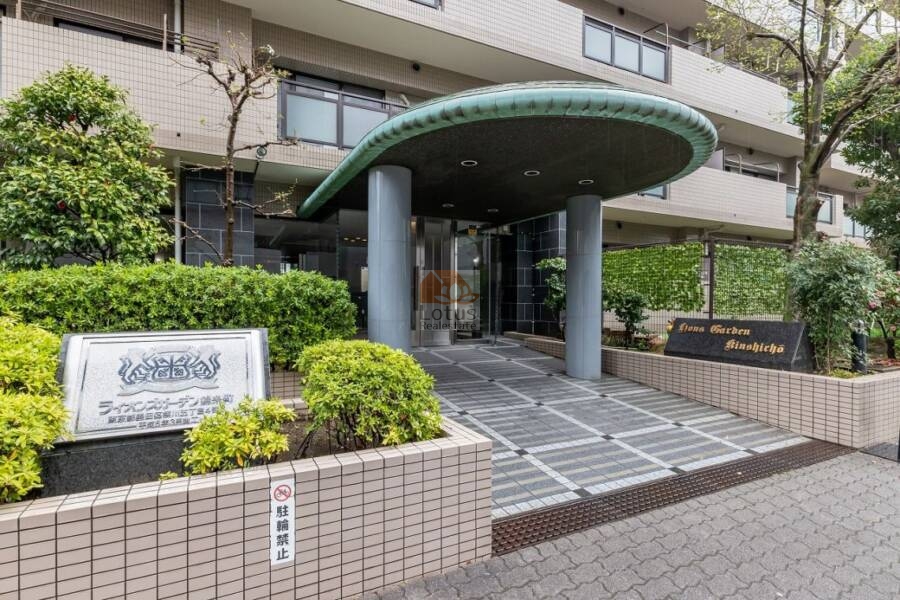 ライオンズガーデン錦糸町エントランス３｜ライオンズガーデン錦糸町のエントランス。深緑色の庇と2本の柱がアクセントになっており、左手には館銘板、右手には英語表記のサインが確認できる。エントランス周囲は植栽で囲まれている。