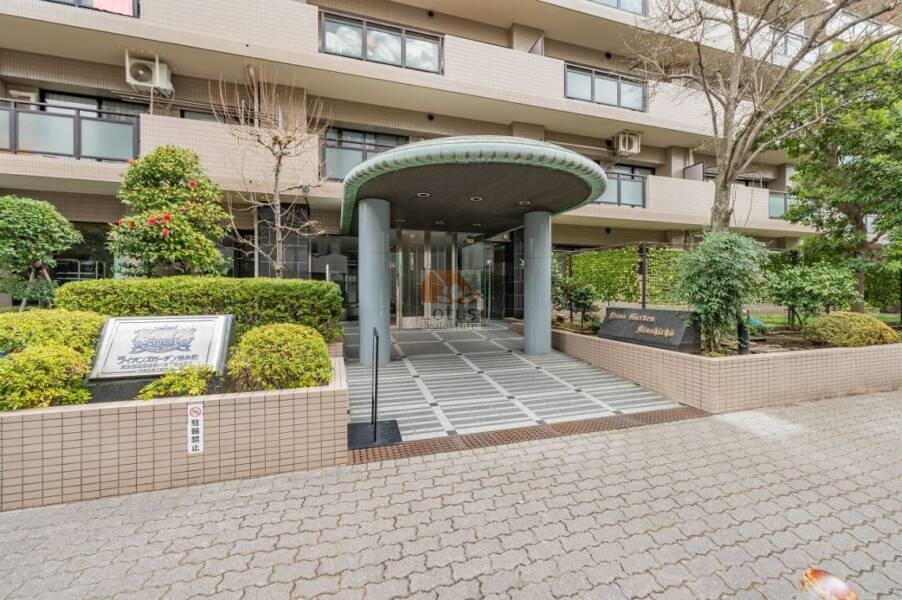 ライオンズガーデン錦糸町エントランス４｜ライオンズガーデン錦糸町のエントランス部分。円形の庇が特徴的なアプローチと、自動ドアが設置されたガラス扉が確認できる。植栽に囲まれた石張りのエントランス空間が整備されている。
