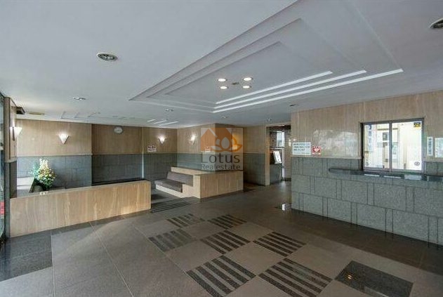 ライオンズガーデン錦糸町共用部１｜ライオンズガーデン錦糸町の共用部の様子。グレーと木目調のパネルで仕上げられたロビー内には、カウンターや郵便受けが設けられている。天井にはダウンライトが多数配置されている。
