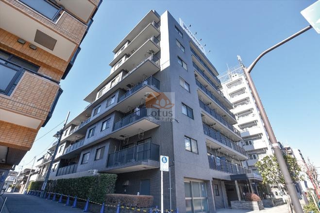 落ち着いたグレーのタイル張り外観で、直線的なデザインが強調されています。バルコニーはガラス手すりと金属フレームで統一され、道路沿いの植栽が足元を彩っています。ステラレジデンス高円寺は、平成7年築、7階建てのマンションです。