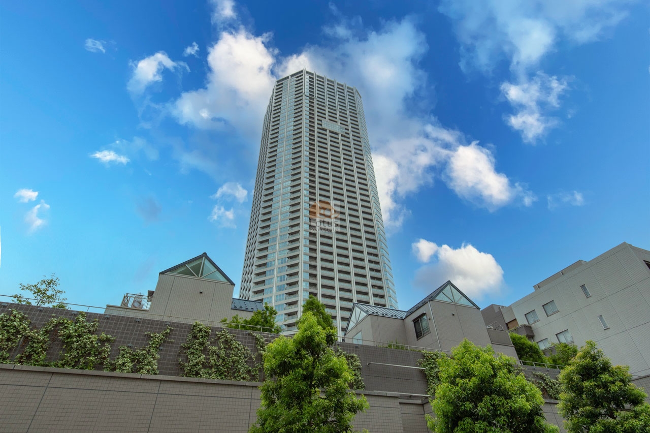 雲が流れる青空を背景に、地上55階建ての超高層タワーがそびえ立っています。低層部には緑化された壁面とガラス屋根の構造が連なり、街並みに調和しながらも存在感を放っています。富久クロスは、平成27年築、55階建てのタワーレジデンスです。