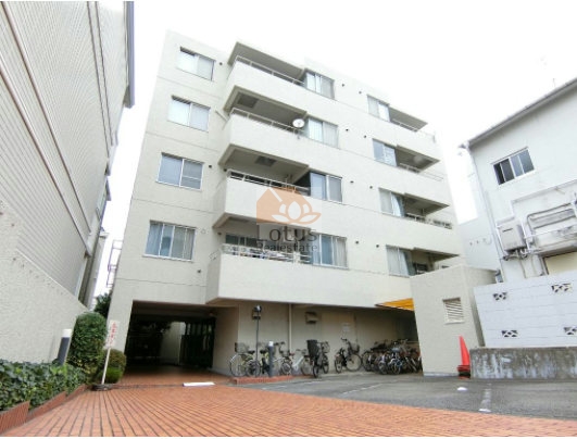池尻ハウスの外観。全5階建の低層マンションで、シンプルなホワイト系ファサードが落ち着いた印象。屋根付きの駐輪場とゆとりあるエントランスアプローチが整い、日常の出入りもスムーズ。前面スペースには複数の自転車が停められ、都市生活者に適した利便性を備えています。池尻ハウスは、昭和56年築、5階建てのマンションです。
