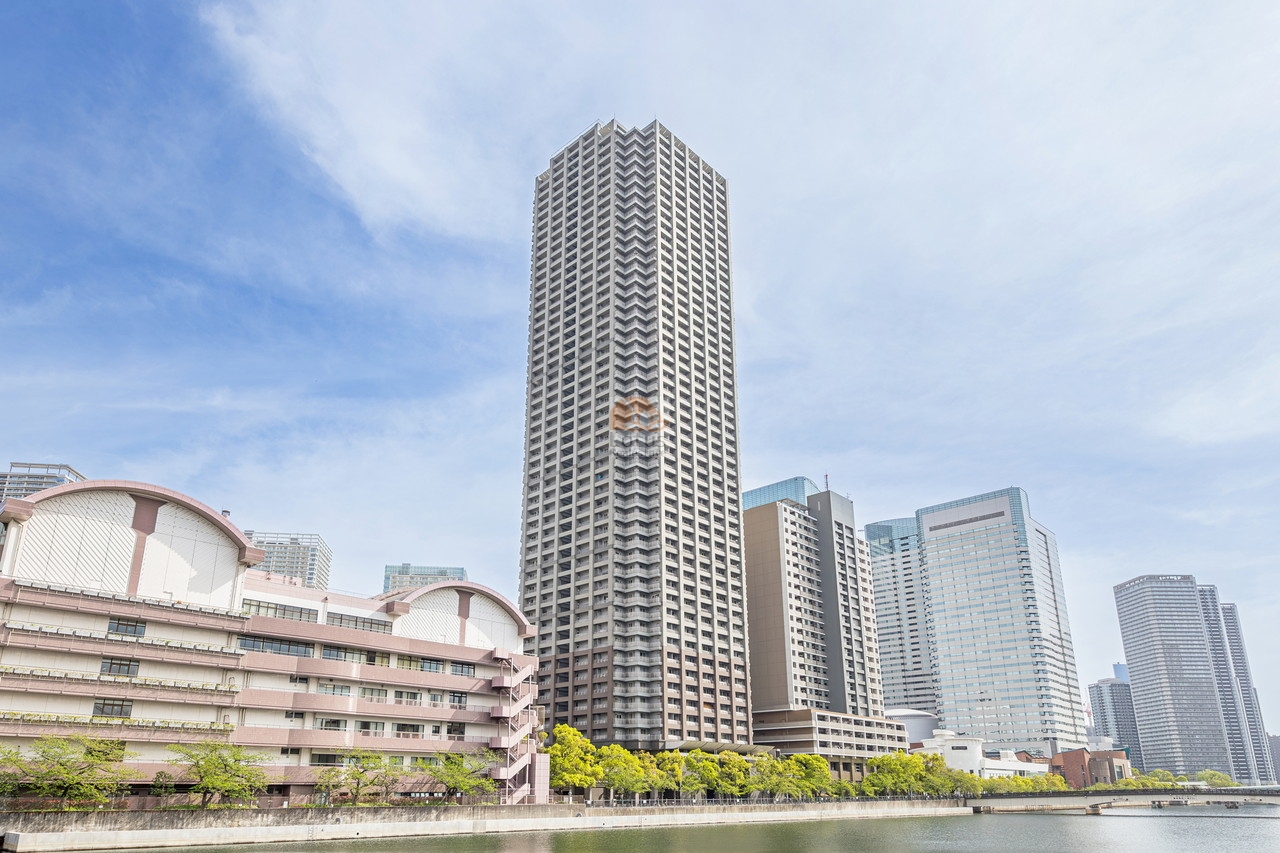 運河沿いにそびえる50階建の高層タワー。建物全体はグレーを基調とし、規則正しいバルコニーラインが空に向かって整然と並んでいます。周囲には水辺の緑とオフィスビル群が広がり、都市景観の一部として調和しています。