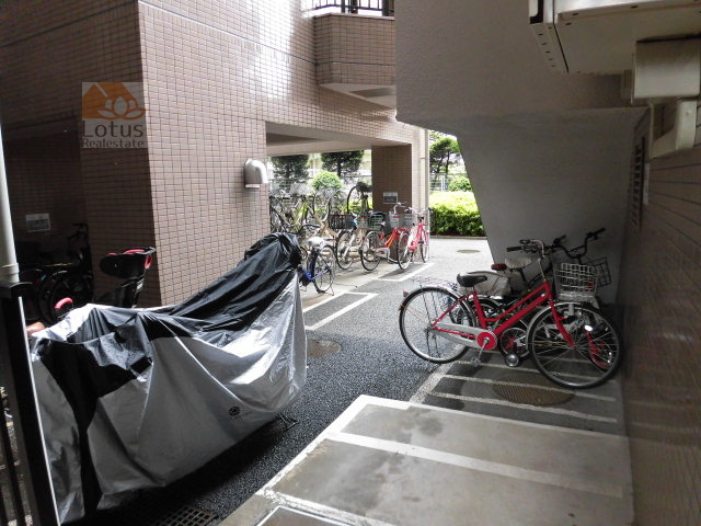 バームハイツ五反野外観 (1)｜駐輪スペースです。共用部には自転車が多数駐輪されているエリアがあり、バイクも駐輪されています。周囲には植栽があります。