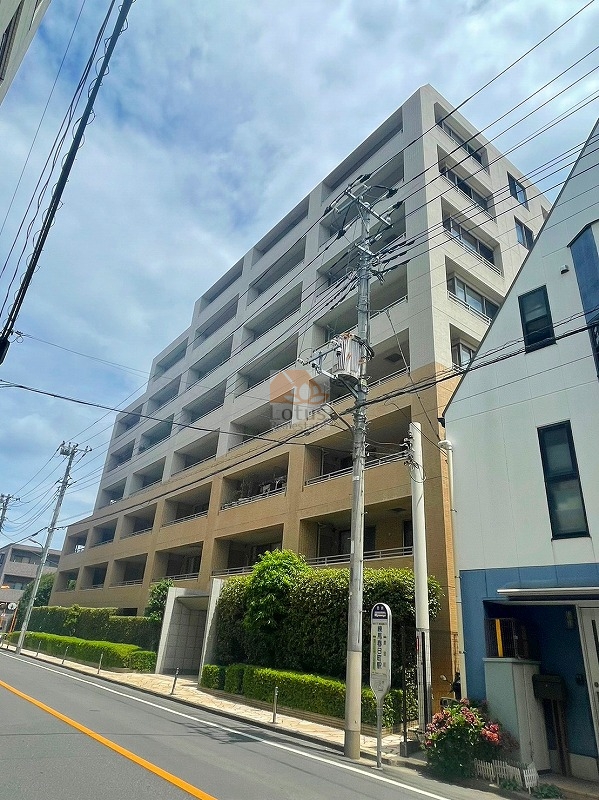 ファストジュール練馬春日町の外観。落ち着いたベージュ系タイル貼りの外壁が印象的で、街並みに自然に溶け込みます。並木や植栽が歩道に沿って整えられており、帰宅時にふっと安らぎを感じられる佇まいです。ファストジュール練馬春日町は、平成13年築、8階建てのマンションです。