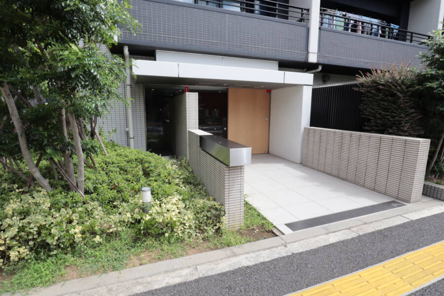 レーベン北千住エアクロスタワーエントランス11｜レーベン北千住エアクロスタワーのエントランスアプローチ。植栽に囲まれた落ち着きある導線が来訪者をやさしく迎え、タイル張りの床と壁が清潔感を保っています。シンプルながらも品のある印象です。
