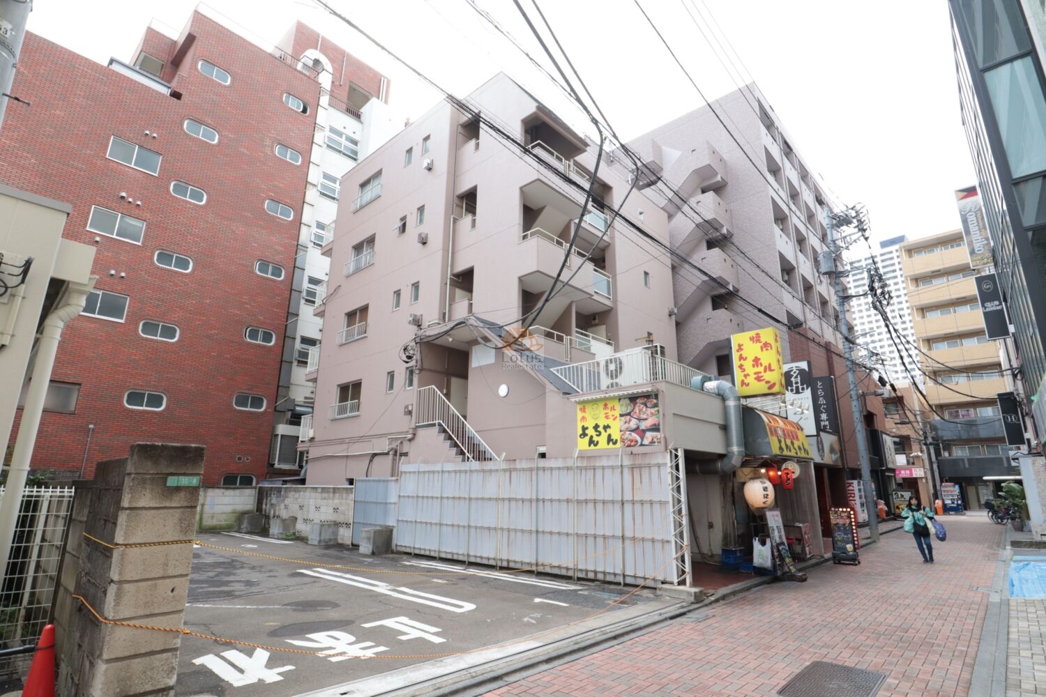 駅前商店街に面したメゾン万里の外観です。短い距離感で店舗が連なり、人の動きが途切れない様子が伝わってきます。歩道の舗装が整い、周囲の建物と近接した立地ゆえに、生活の音や人通りを身近に感じながら暮らす日常が思い浮かぶようです。
