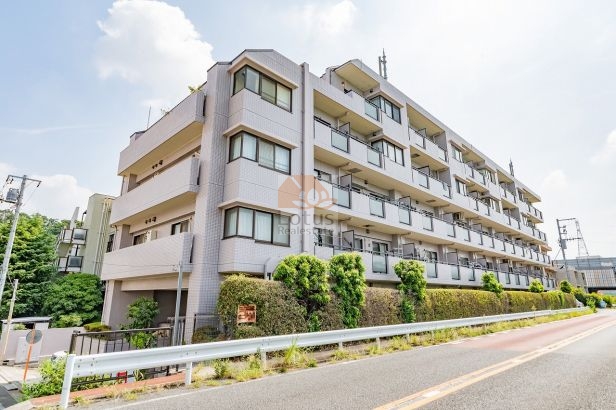 道路沿いから見た外観です。白を基調としたタイル貼りの外壁が整い、4階建ての建物が横に広がっています。手前には植栽が並び、建物の印象を柔らげています。セザールリバーサイド上野毛は、平成10年築、5階建てのマンションです。