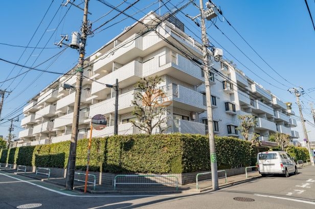 白系タイル張りの外観が通りに対して端正な印象を与え、敷地周囲の植栽が視線をやわらかく受け止めます。角地に近い配置で建物全体が見渡しやすく、前面道路の距離感にも余裕があり、若林駅徒歩9分という立地ながら落ち着いた空気が漂います。