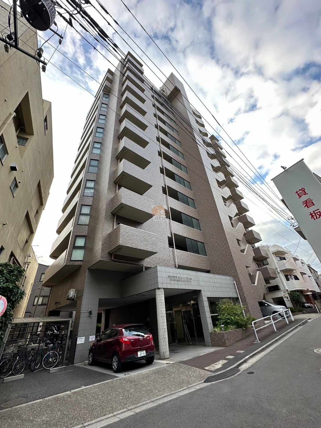 日神パレステージ板橋本町第６は、平成7年築、地上12階建のタイル貼り外観で、ブラウンとグレーを基調とした落ち着きある印象。エントランスには庇付きの車寄せと屋根付き駐輪場があり、暮らしの快適性と利便性が感じられる設計。