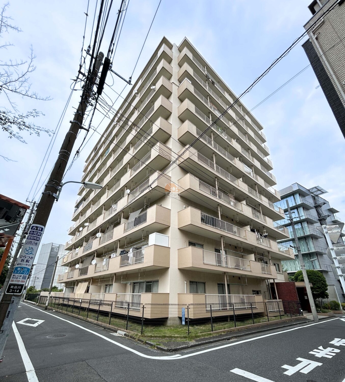 南西角から見た建物全景です。ベージュ系の外壁に整列したバルコニーが並び、地上10階建ての均整の取れた外観です。通りに面した角地に立地し、建物のファサードが交差点方向に開いています。