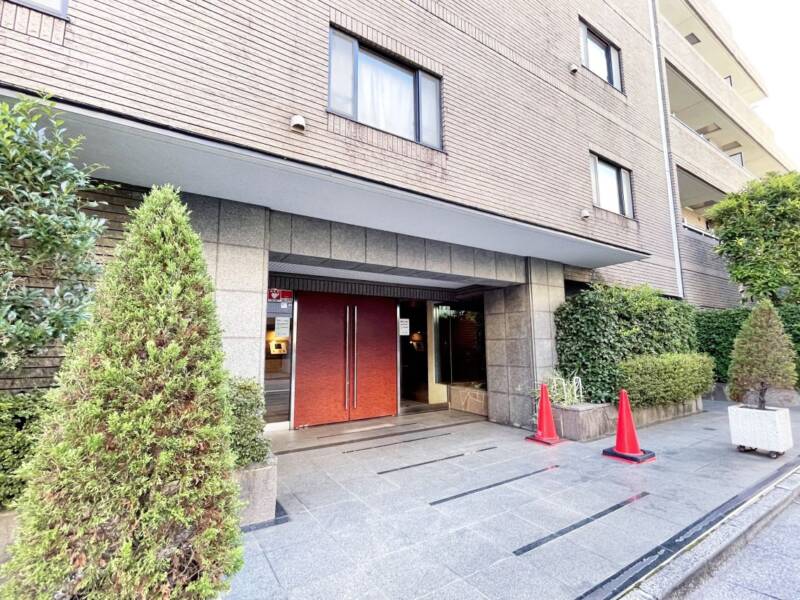 牛込南町クィーンヒルズエントランス１｜ベージュ系の外壁で、エントランス前は広くゆとりがあり、グレーの石張り、重厚感のあるつくりです。