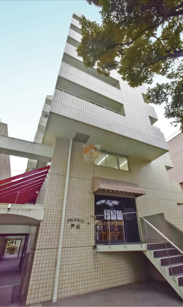 白いタイル貼りの外観が印象的で、直線的なフォルムが都会的な印象を与えます。建物の足元には緑が残され、硬質な素材のなかに柔らかい光を感じられます。