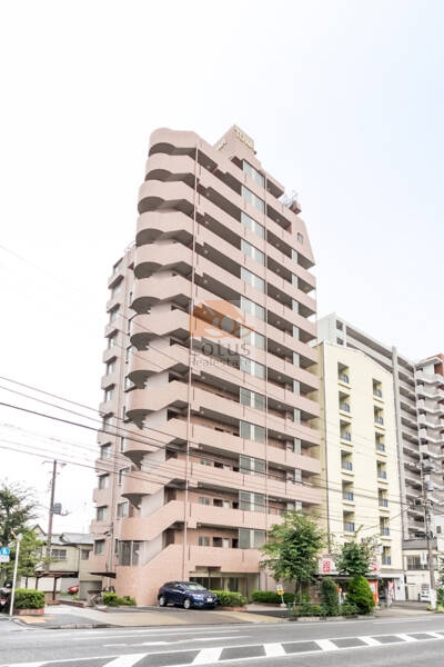 明治通り沿いに立つSRC造14階建ての外観です。タイル貼りの落ち着いた色調が縦のラインを強調し、通りの交通量を受け止めながらも建物全体の輪郭は穏やかで、都市幹線沿いにありながら視覚的な圧迫感を抑えた構成といえます。