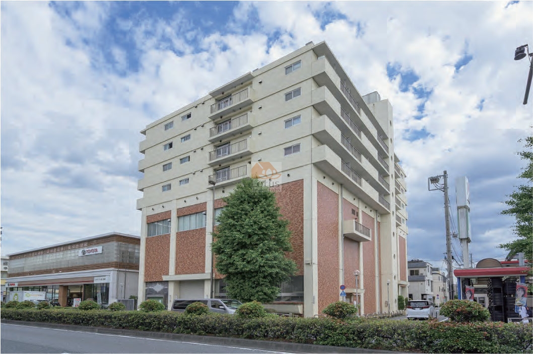 川越街道沿いの商店やショールームに隣接する角地に建つ、桜川グレースマンションの外観です。下層階は赤みを帯びたタイル調の壁面で、大きな開口部が設けられており、上層階はシンプルな白系の外壁です。道路沿いには植え込みと並木が整備され、青空を背景にした全体像からは、住居と商業の機能が共存する建物の姿が伝わってきます。桜川グレースマンションは、昭和49年築、7階建てのマンションです。