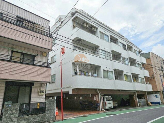 第一東個マンション外観１.jpg 立会川駅徒歩3分の通り沿いにあり、白い外壁が淡く光を受けて輪郭を整えている様子が印象的です。新浜川公園が徒歩2分にあることを踏まえると、駅前の利便と小さな公園の落ち着きがどちらも生活導線に入りやすい配置といえます。建物下部のピロティには駐車スペースや駐輪スペースが収まり、用途が整理されたつくりで日常の動きが無理なく完結します。第一東個マンションは、昭和53年築、6階建てのマンションです。