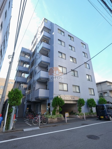 セザール大森の外観。淡いブルーグレーのタイルで仕上げられた外観は、周囲の建物と調和しながらも明快な輪郭を保っています。ファサードには立体的なバルコニーがリズムを生み、通りに面した植栽や自転車置場が整然と配置され、日常動線の落ち着きを演出しています。セザール大森は、平成7年築、7階建てのマンションです。