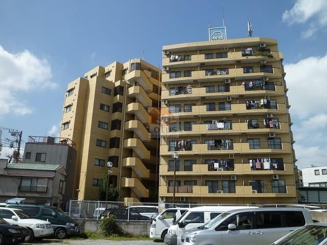 グローリア初穂ときわ台の外観。ベージュ系タイル貼りの9階建SRC造で、ゆったりした中規模マンションならではの落ち着いた佇まい。敷地前には駐車スペースも確保され、生活利便性を高めている。グローリア初穂ときわ台は、昭和60年築、9階建てのマンションです。