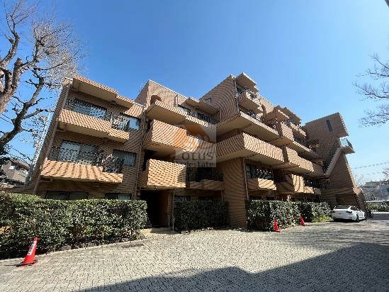東急ドエルアルス弦巻の1号棟の外観。タイル張りのファサードと段状に配置されたバルコニーが、独自のリズム感ある建築美を形成。落ち着いた色調と植栽が調和し、邸宅らしい風格を醸し出しています。東急ドエルアルス弦巻は、昭和54年築、6階建てのマンションです。