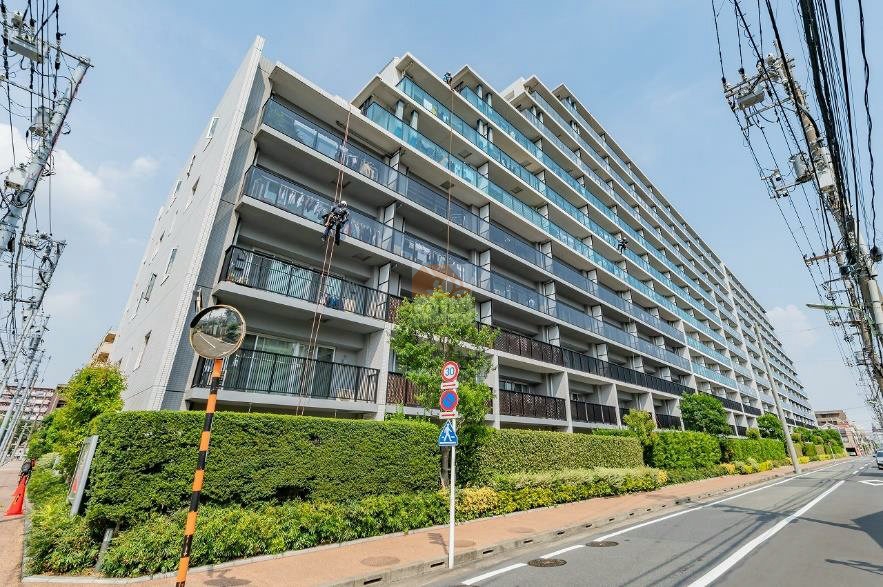 広がる外観はガラス手すりと整然と並ぶバルコニーが特徴的で、縦に伸びる建物のラインが都市的な印象を与えています。植栽の緑とともに管理スタッフによる清掃作業が行われている様子も確認でき、日常的なメンテナンスの丁寧さを感じさせます。シティテラス大森西は、平成28年築、11階建てのマンションです。