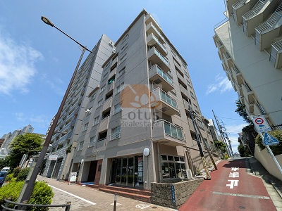 山手通り沿いに立つ8階建ての外観は、直線的なフォルムで街並みに溶け込みつつ、角地らしい視認性を備えています。参宮橋駅・初台駅ともに徒歩7分という距離感が伝わる立地で、歩行者と車の動線が整理された通りに面し、昼間は空が広く感じられるのが印象的です。交通量はありますが、建物のスケールが抑えられているため圧迫感は少なく、都市生活の合理性を静かに支える佇まいといえます。