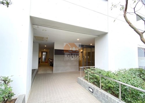 リベルジェ尾久駅前エントランス｜ロープ付きでバリアフリー対応のエントランスアプローチです。屋根付きの空間にはオートロックとガラス扉が設置され、安全性と開放感を両立しています。