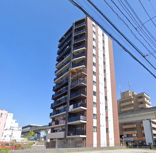 オスピタリテ谷在家の外観全景。赤茶系の外壁と縦に伸びるすっきりしたフォルムが特徴で、全13階建の中高層レジデンス。駅徒歩2分とは思えないほど、空と調和した開放感ある佇まいです。オスピタリテ谷在家は、令和3年築、13階建てのマンションです。