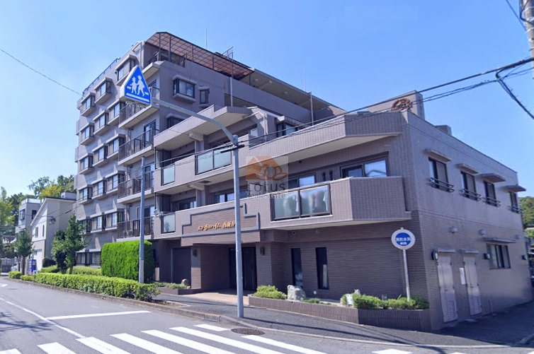 エンゼルハイム西新井の外観全景。角地に建つ安定感のある7階建てマンションで、整った植栽と横断歩道が生活利便性を感じさせる環境。道路沿いに面した明るい印象のファサードも魅力。ベージュ系タイル貼りの外観が、落ち着きある街並みに調和。エンゼルハイム西新井は、平成9年築、7階建てのマンションです。