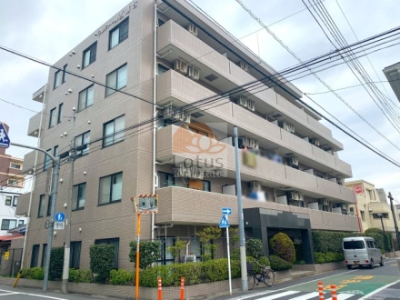 クレアトール西落合の外観。交差点の角地に建つ地上5階相当のタイル貼りマンションです。2方向の道路に面し、1階まわりには生垣や低木の植栽が連続しています。東側には庇付きの出入口が設けられています。クレアトール西落合は、平成7年築、5階建てのマンションです。