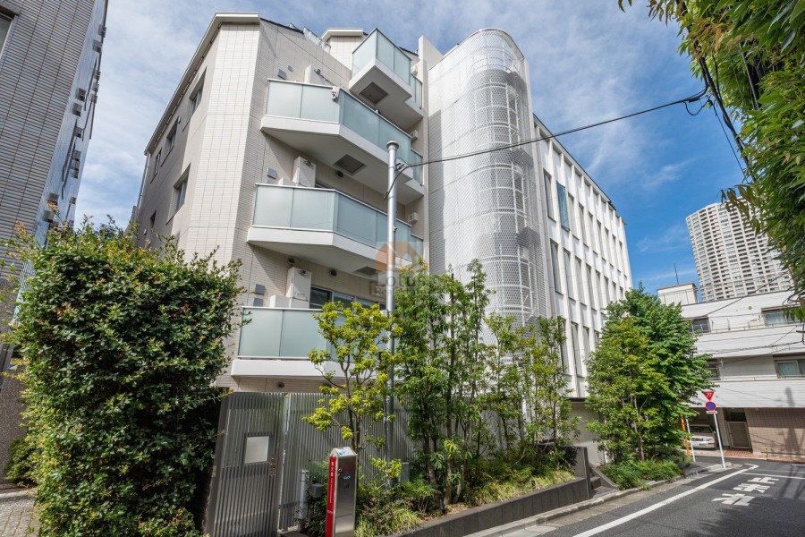 白を基調とした外壁とガラス手すりが調和した7階建の外観で、植栽がエントランス周辺を彩ります。閑静な住宅地の一角にあり、プライバシーとデザイン性を両立した都市型レジデンスです。