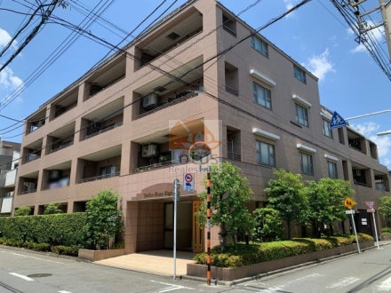 ガーデンホーム久が原の全景が写っています。4階建てのタイル外壁、角部はセットバックしています。歩道側には生垣と低木があります。建物の基壇部には庇付きの開口があり、車道・歩道との取り付きが確認できます。ガーデンホーム久が原は、平成12年築、5階建てのマンションです。