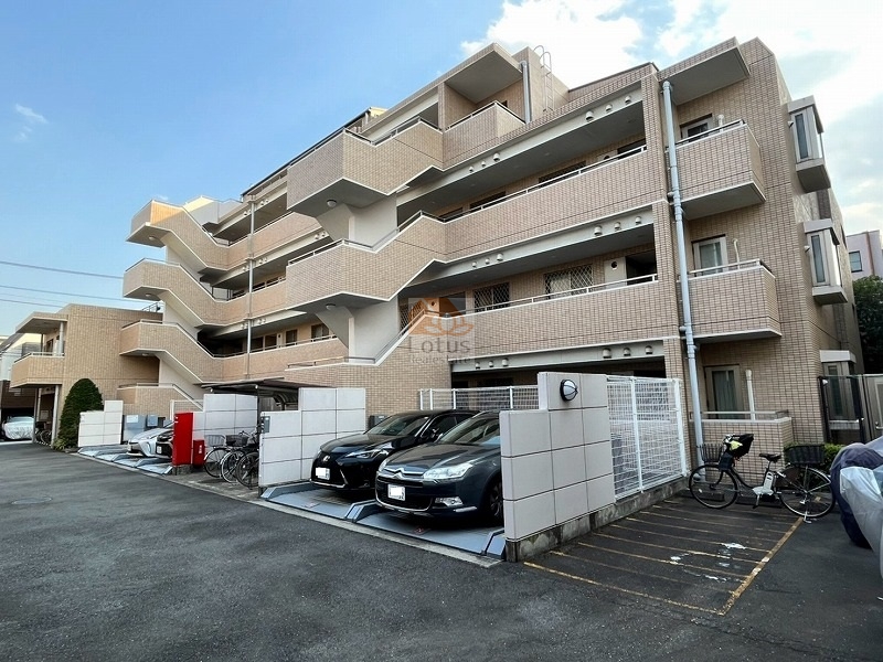 ベージュ系タイルが穏やかに陽光を反射し、低層のフォルムが住宅地の空気に自然に溶け込んでいます。角地に面した配置で、通風と採光のバランスが理にかなっています。敷地内には平置き駐車場と駐輪スペースを整え、住戸数22戸に対してゆとりある構成です。