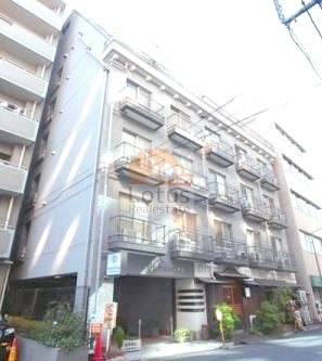 靖国通りから少し入った通りに建つ外観で、グレーを基調とした低中層の建物が確認できます。道路側には複数の小さなバルコニーが整然と並び、街並みに落ち着いた印象を与えています。九段アビタシオンは、昭和５３年築、８階建てのマンションです。