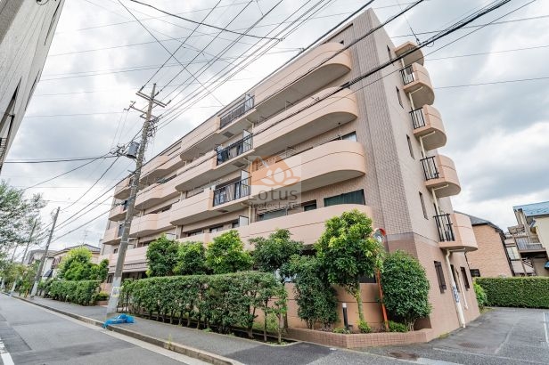 穏やかな住宅街に面した外観です。5階建ての低層フォルムに、やわらかなベージュ系タイル貼りの外壁と曲線ラインが特徴的です。前面の植栽が通り沿いに並び、道路からの視線をやわらげています。